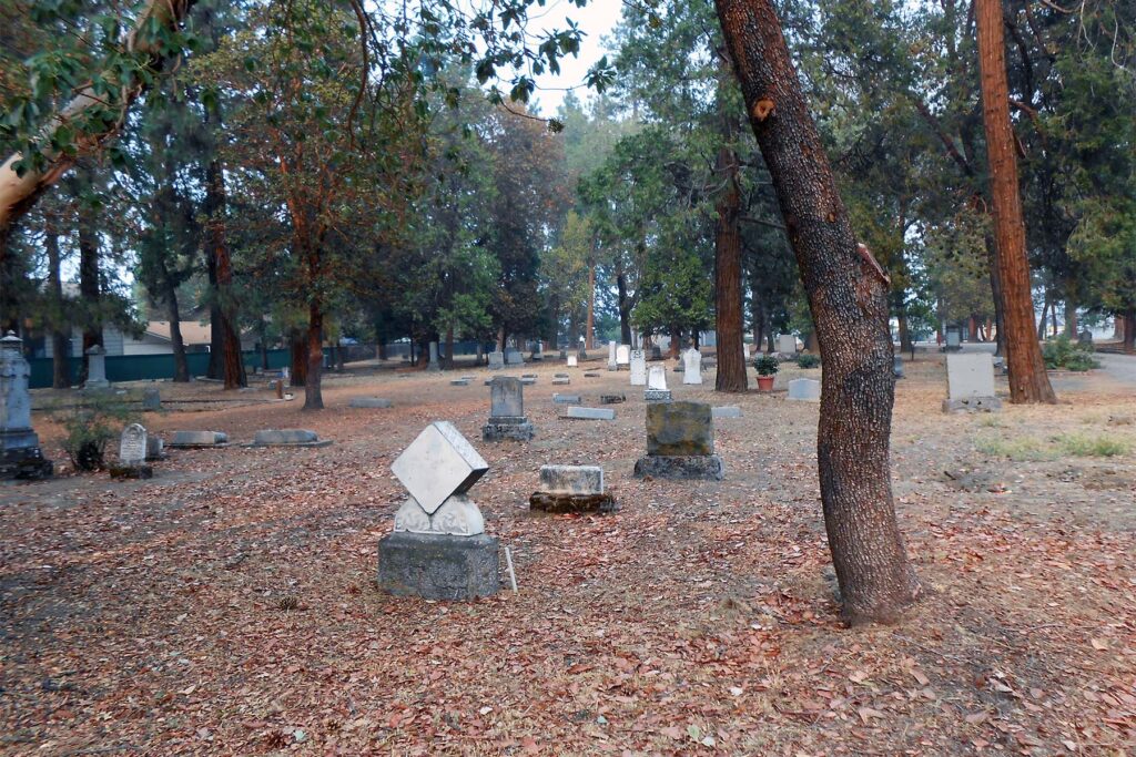 Many headstones laying in a cemetery with trees