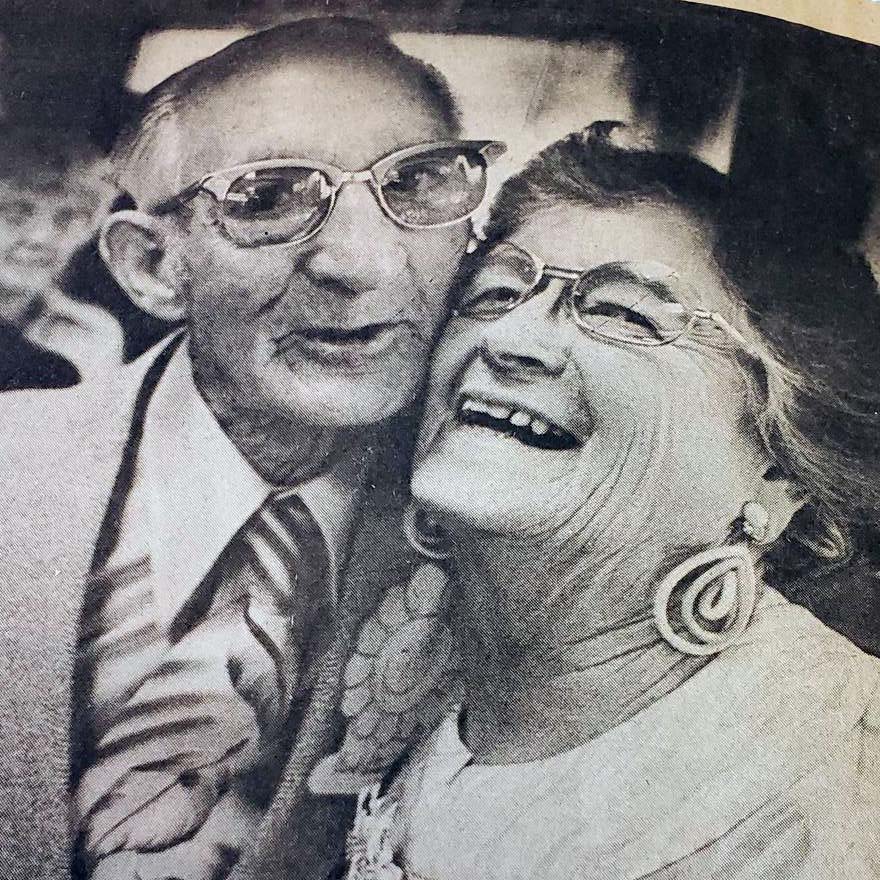 A black and white photo of an elderly couple laughing and smiling for the camera